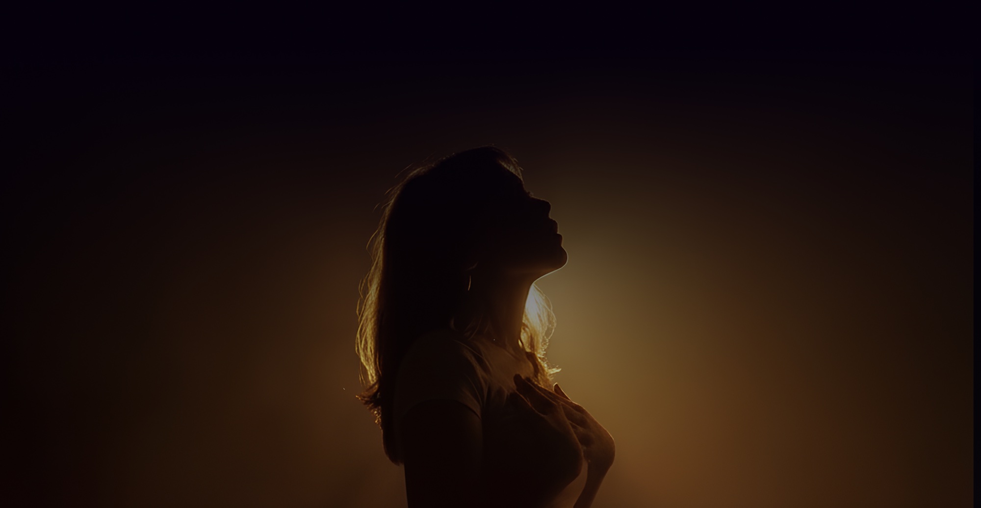 A woman standing in golden light with her hand on her heart