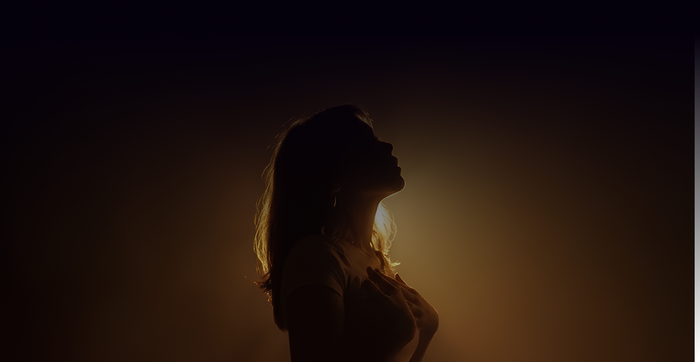A woman standing in golden light with her hand on her heart